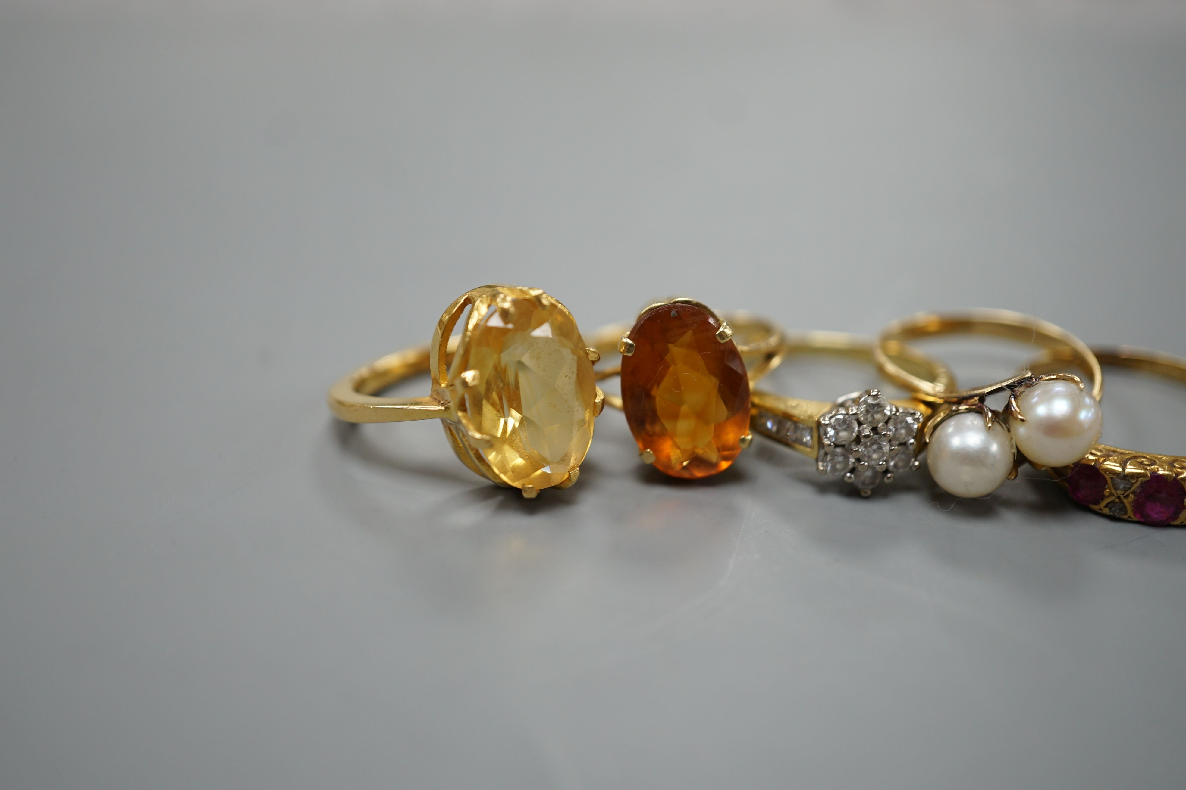 Five assorted gold and gold coloured metal dress rings, comprising a two stone cultured pearl stamped 18k, size L, an 18ct gold diamond cluster, size L, an unmarked citrine?, an 18ct orange stone, size L and an early 20t